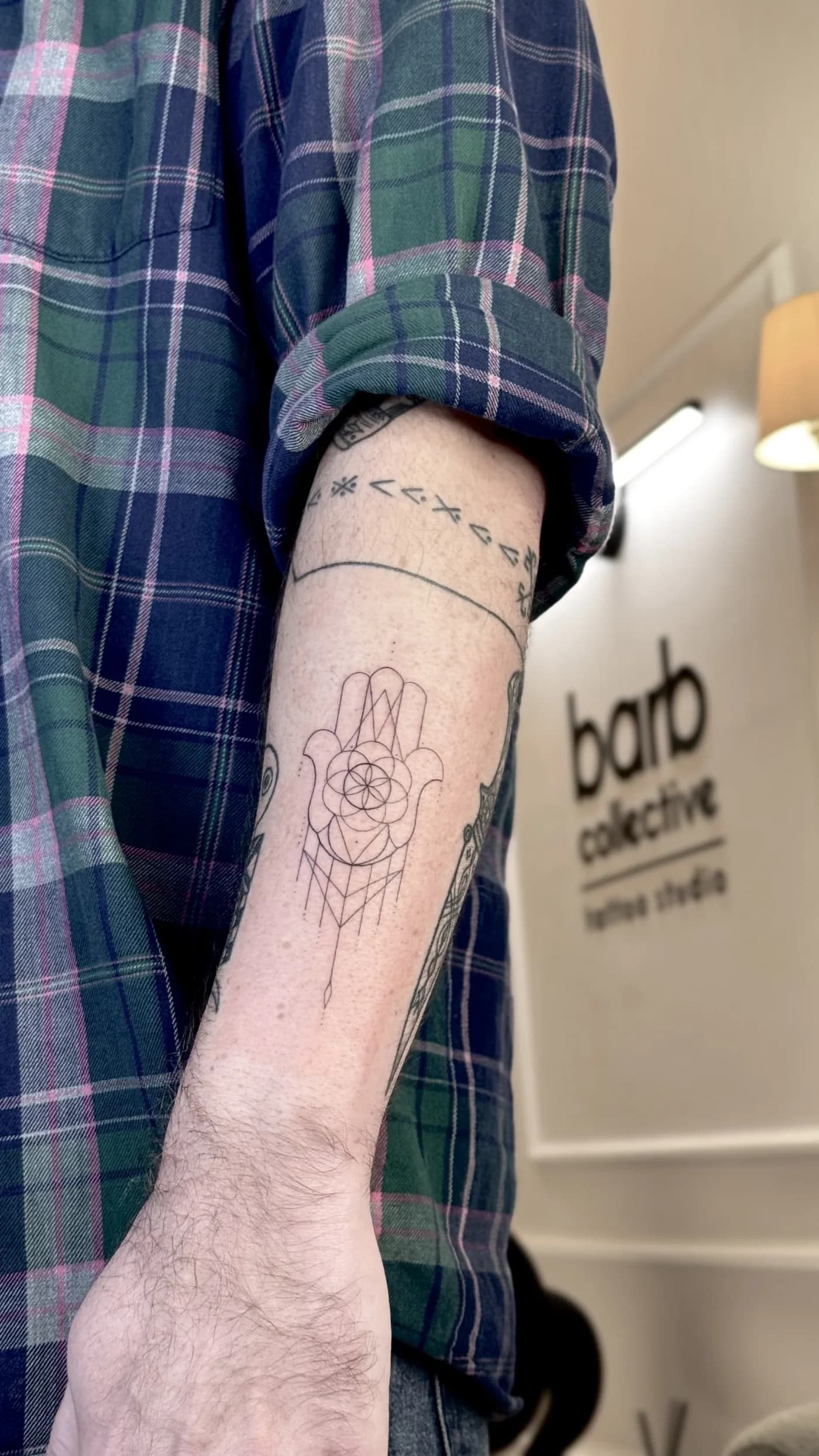 A fine-line hamsa and geometric pattern along the forearm